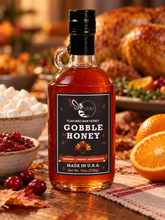 Load image into Gallery viewer, Firebee Gobble Honey 19oz glass bottle on a Thanksgiving table beside cranberry sauce, marshmallows and an orange